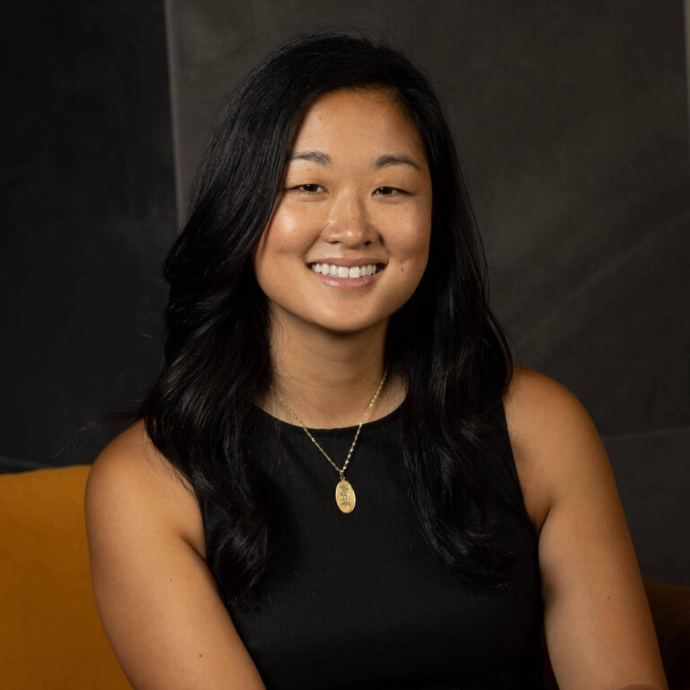 Woman smiling in black dress against dark background