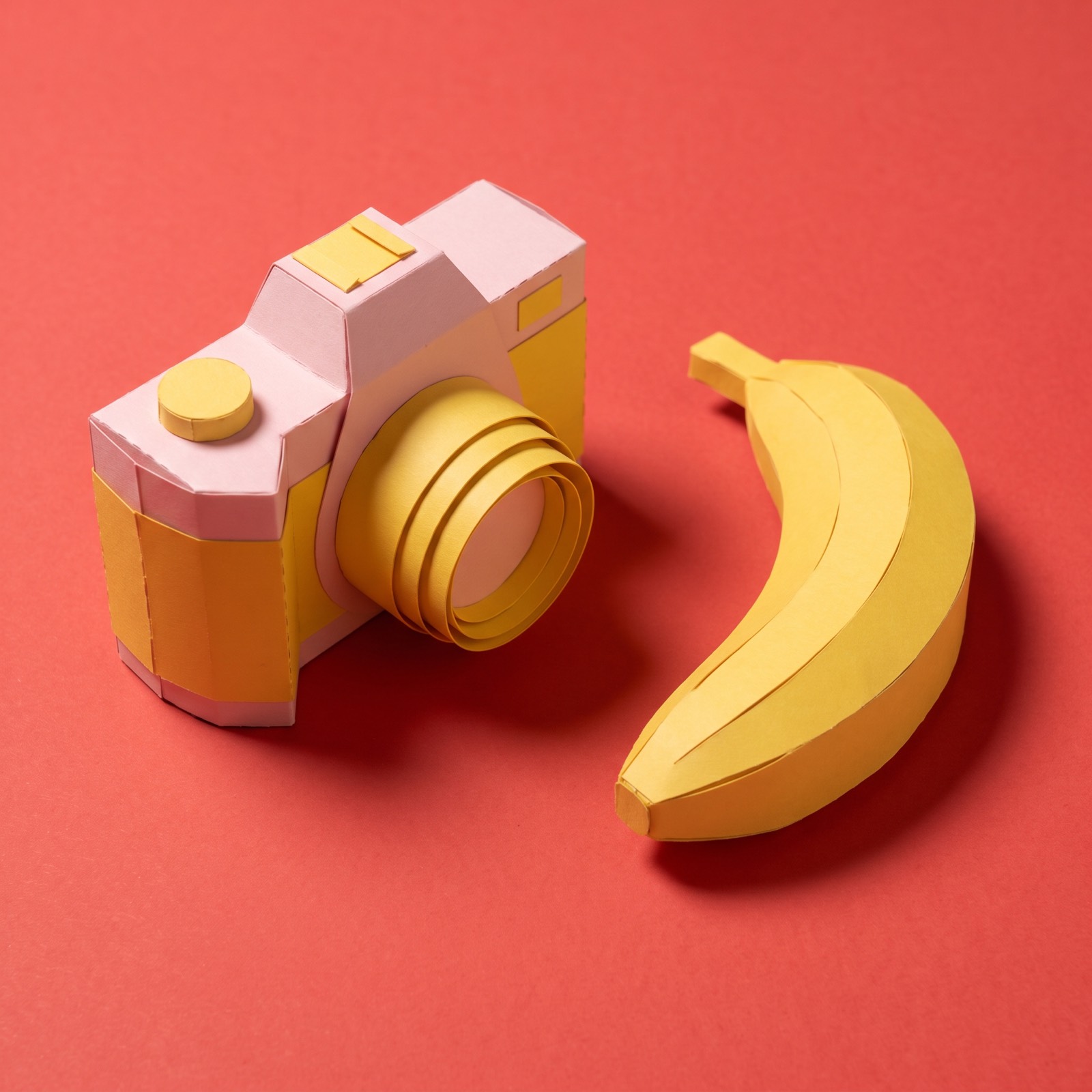 Paper sculpture of a camera with a banana lying beside it