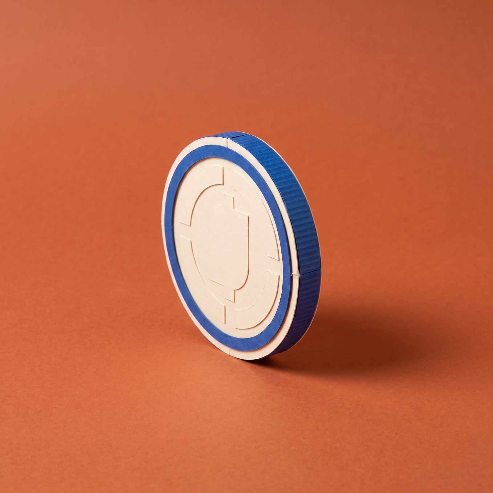 Paper sculpture of a single coin with a raised rim and a ridged edge, balanced on its thin edge