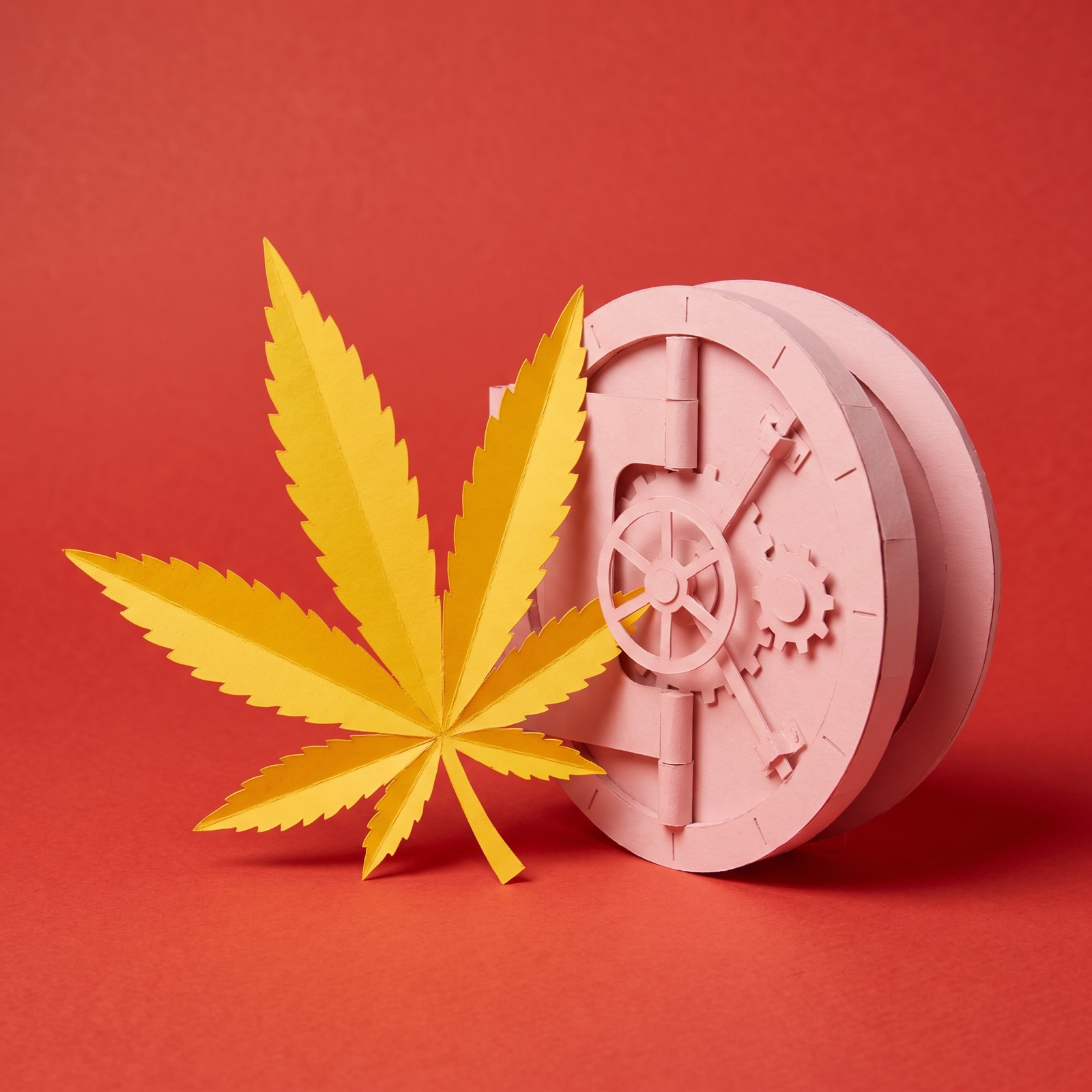 Paper sculpture of a cannabis leaf resting against a round bank vault door