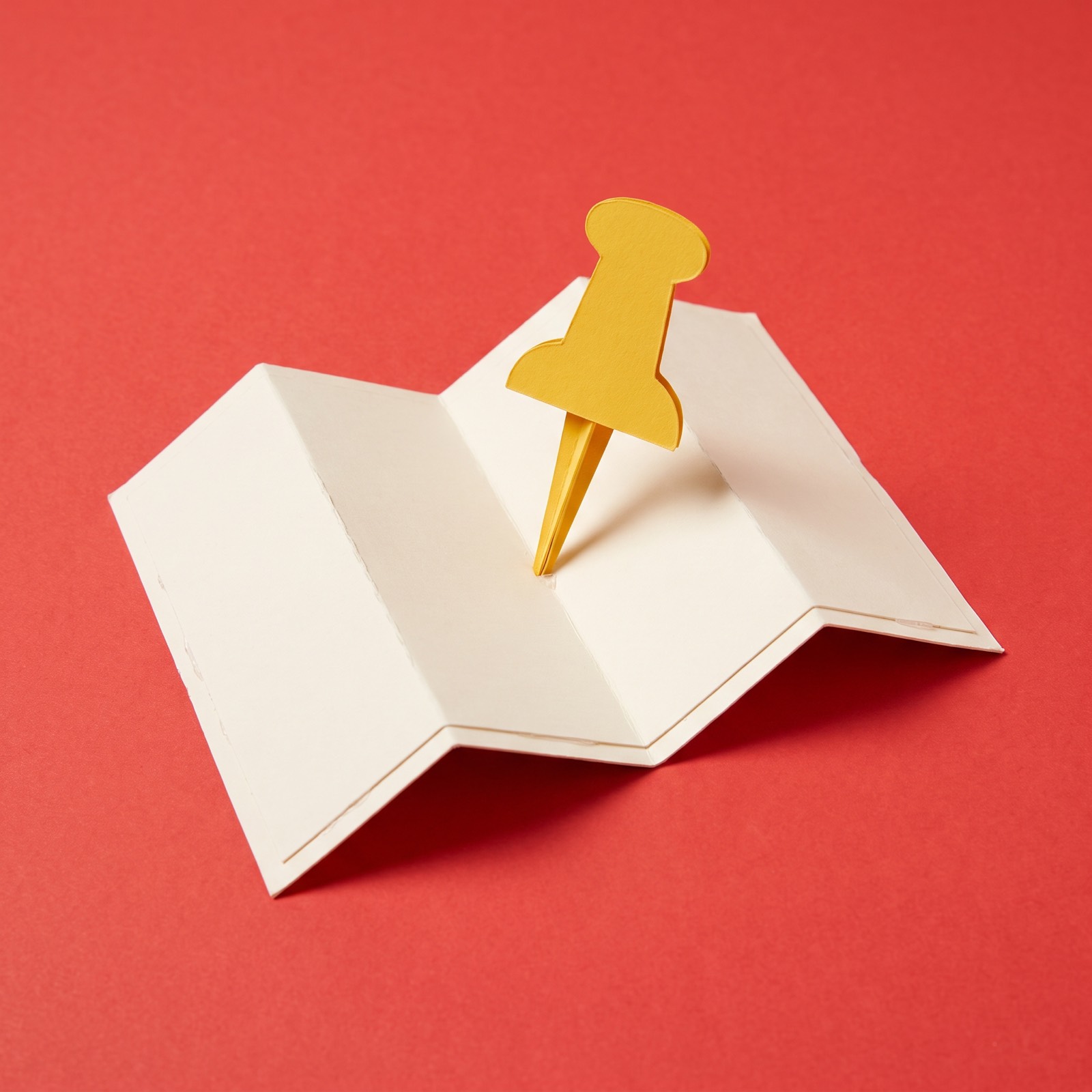 Paper sculpture of a map pin pushed into a folded map