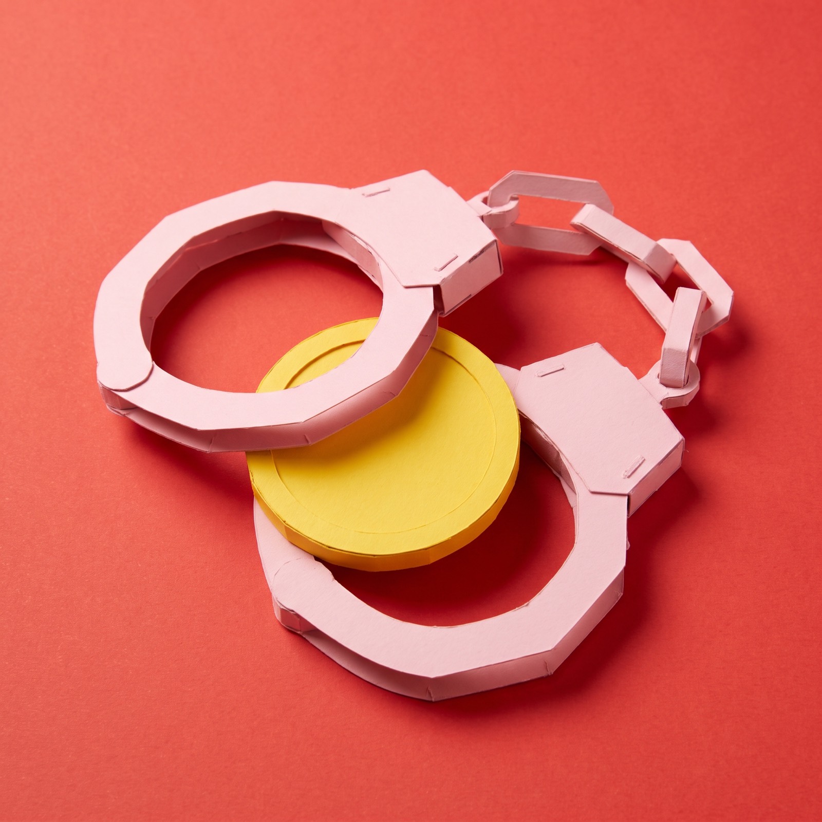 Paper sculpture of a pair of handcuffs looped around a single coin