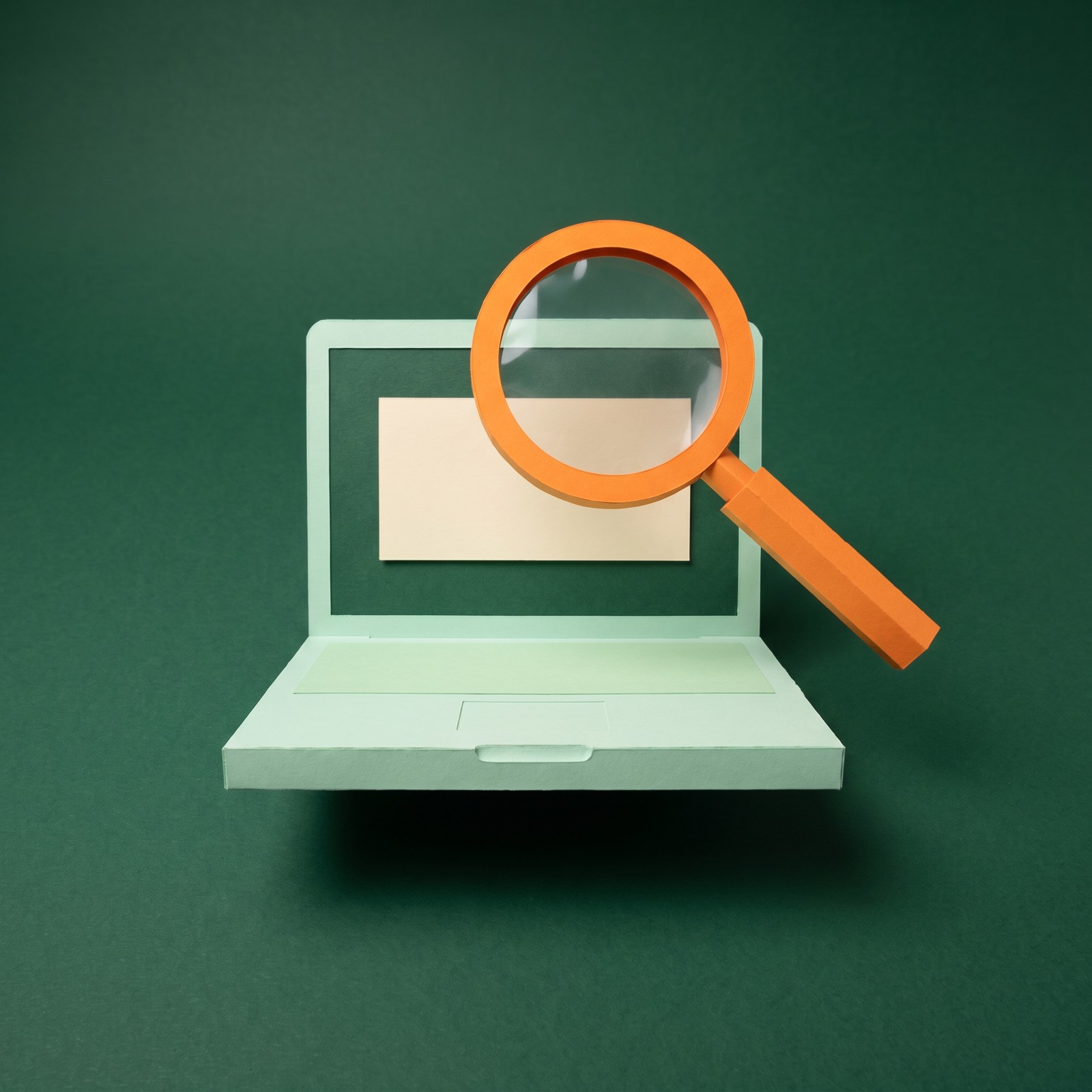 Paper sculpture of a magnifying glass held over an open laptop