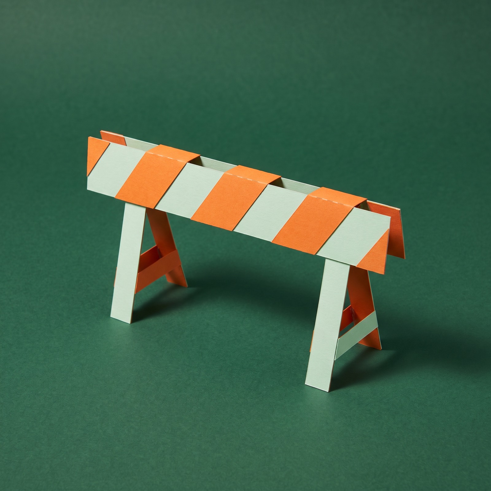 Paper sculpture of a striped road barrier on two stands