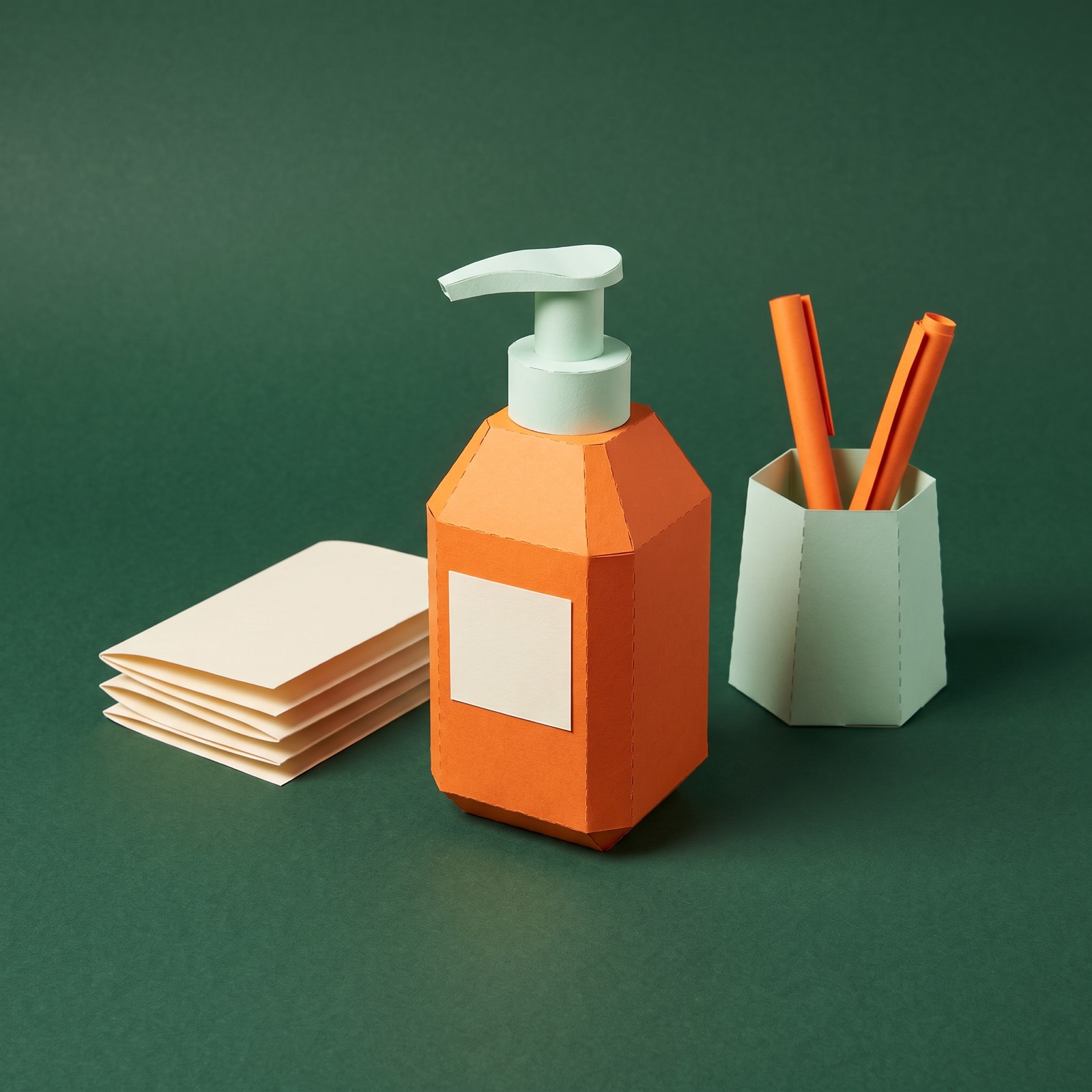 Paper sculpture of a pump bottle of hand sanitizer standing on an office desk