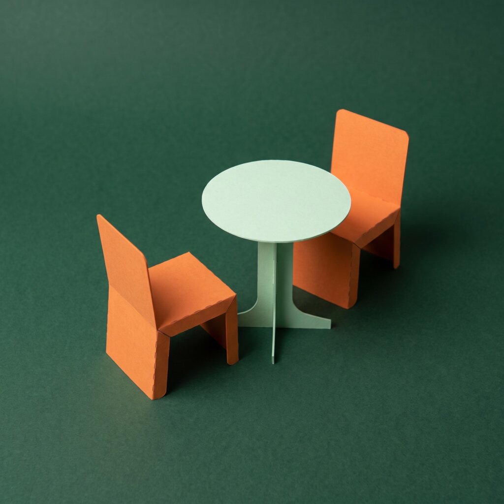 Paper sculpture of two chairs at a small table, one pushed back from it