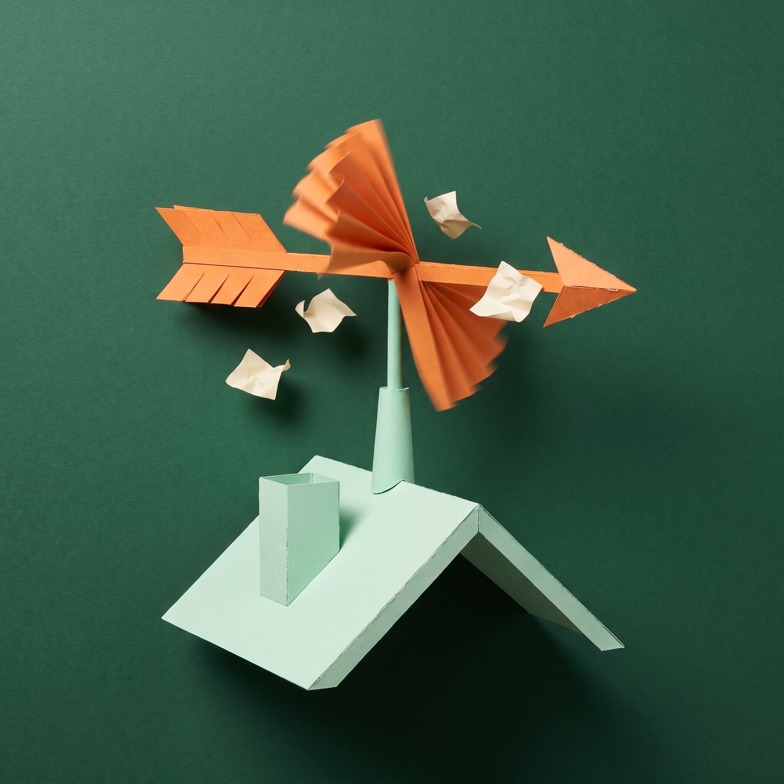 Paper sculpture of a weathervane spinning on a rooftop