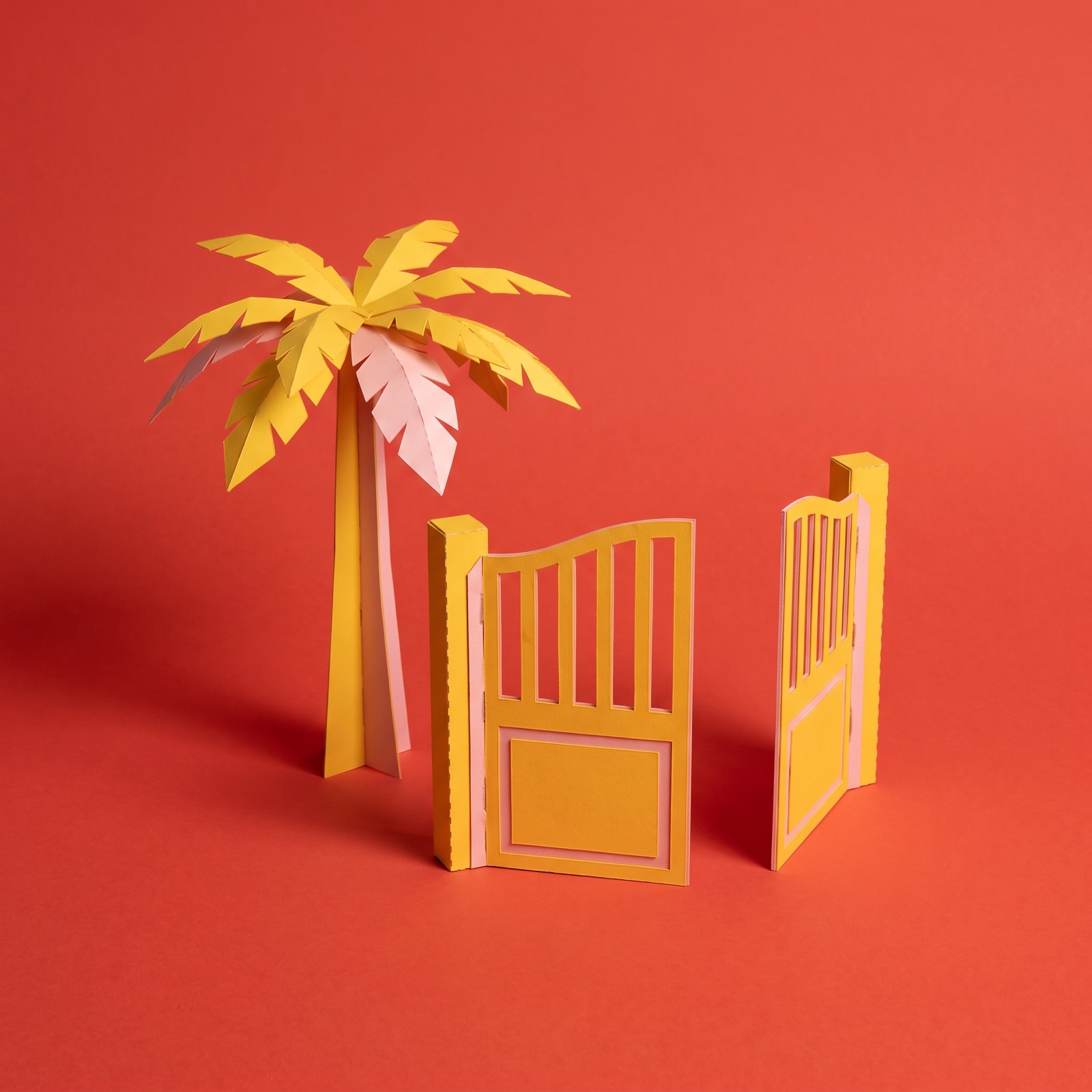 Paper sculpture of a palm tree beside a garden gate standing wide open