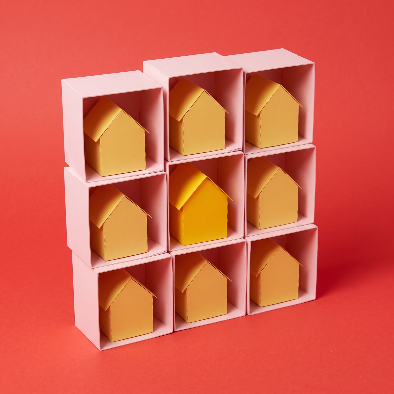 Paper sculpture of a set of stacked cubby shelves with one small house in each compartment