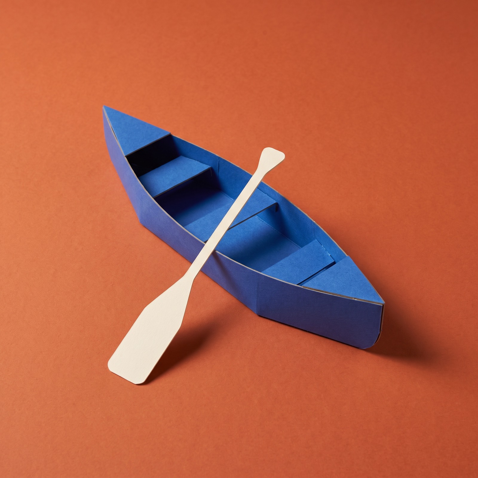 Paper sculpture of a one-person canoe with its paddle
