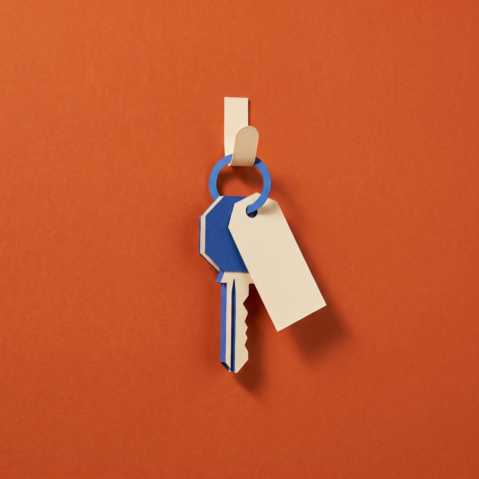 Paper sculpture of a house key with a blank tag, hanging on a hook