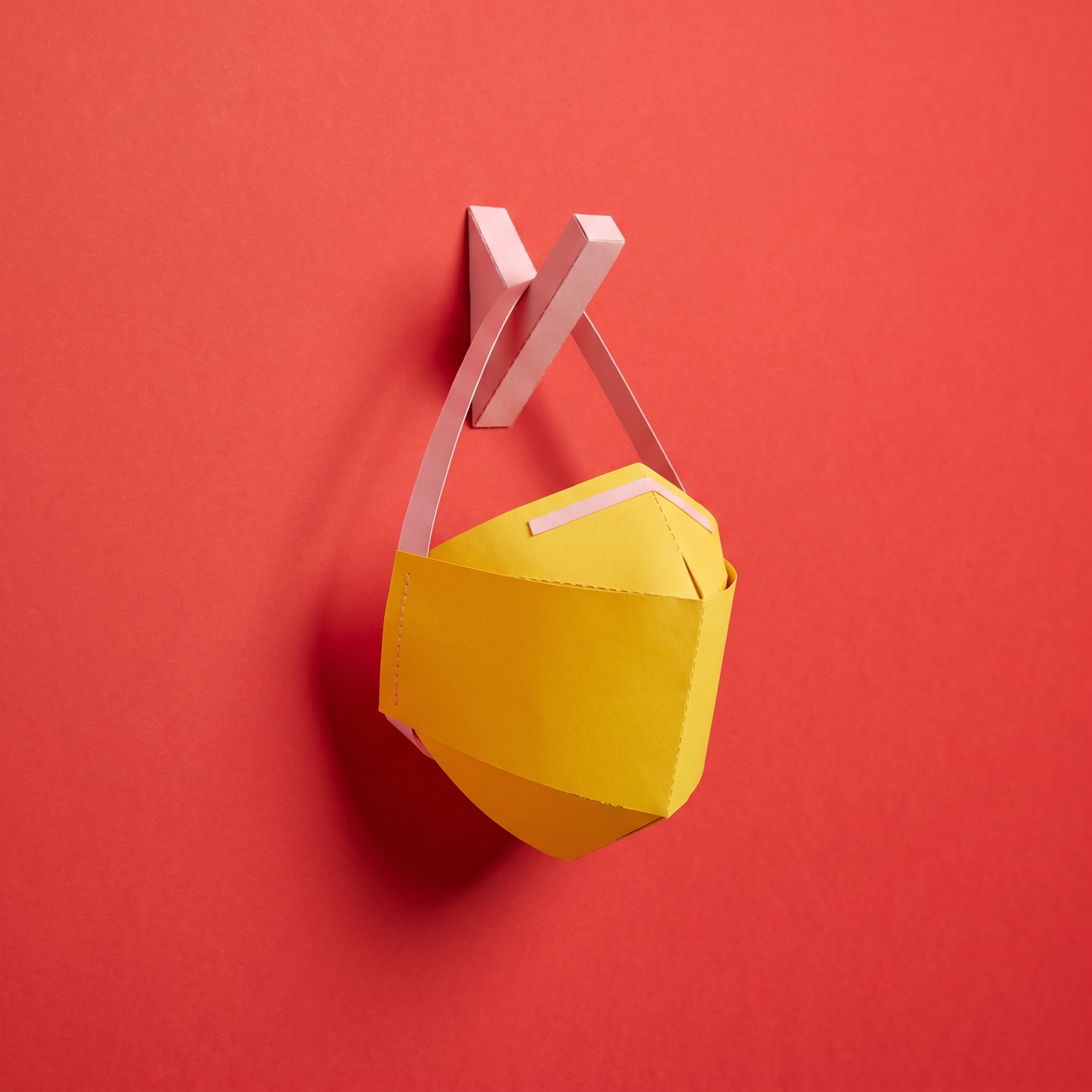 Paper sculpture of a face mask hanging from a coat hook