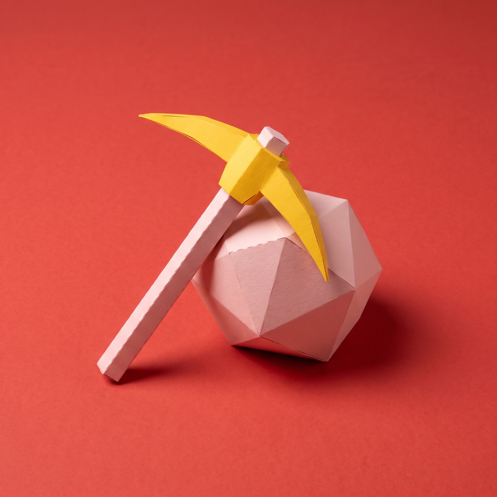Paper sculpture of a pickaxe leaning against a boulder