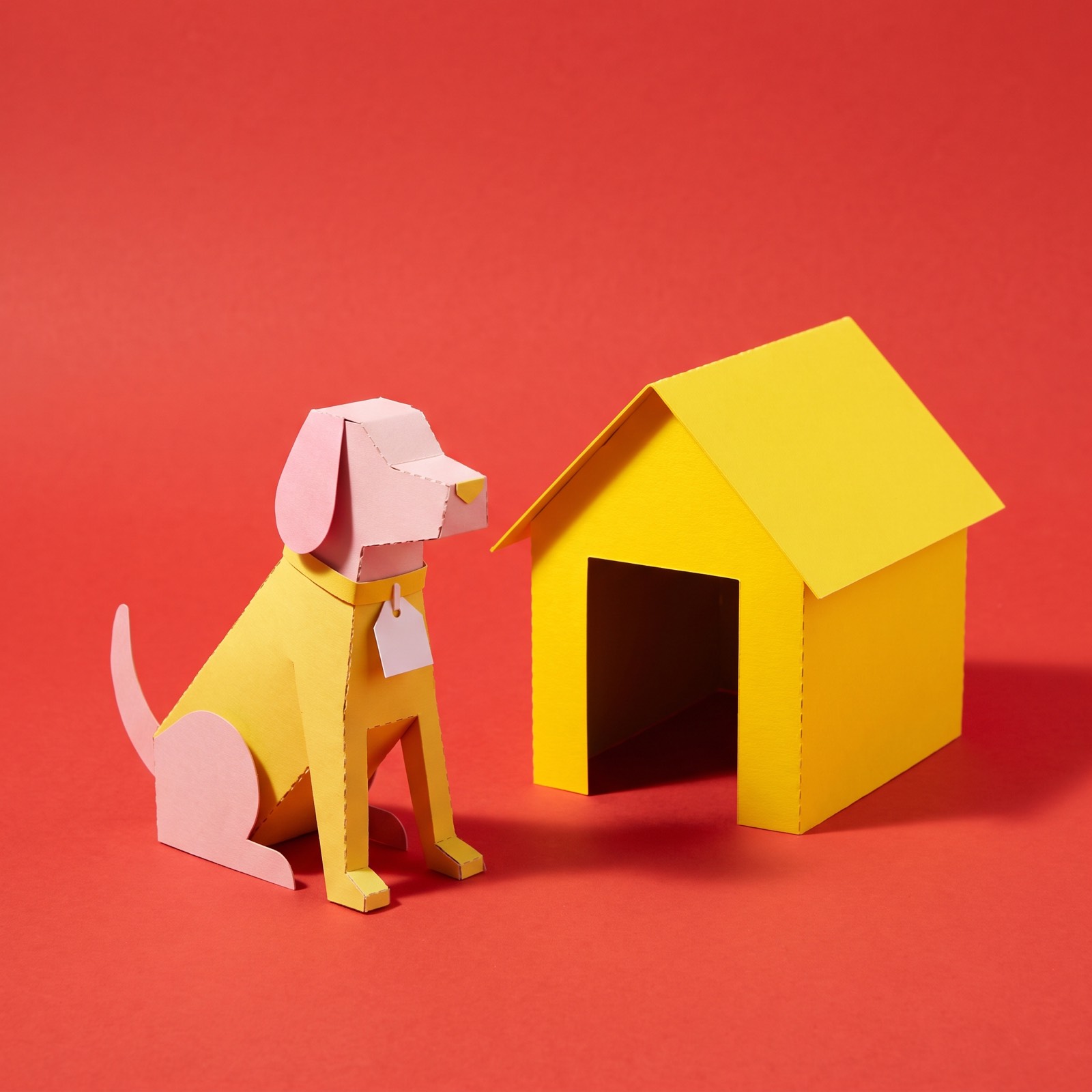 Paper sculpture of a guard dog sitting alert beside its kennel