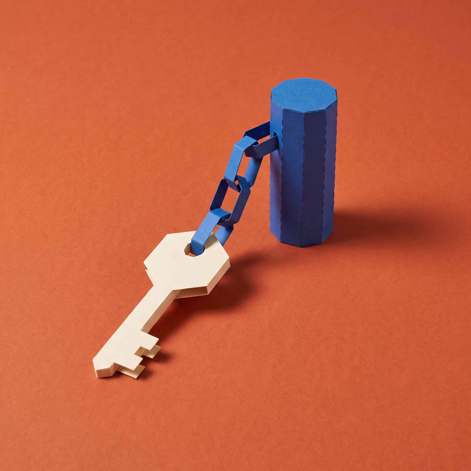 Paper sculpture of a key on a short chain fixed to a post
