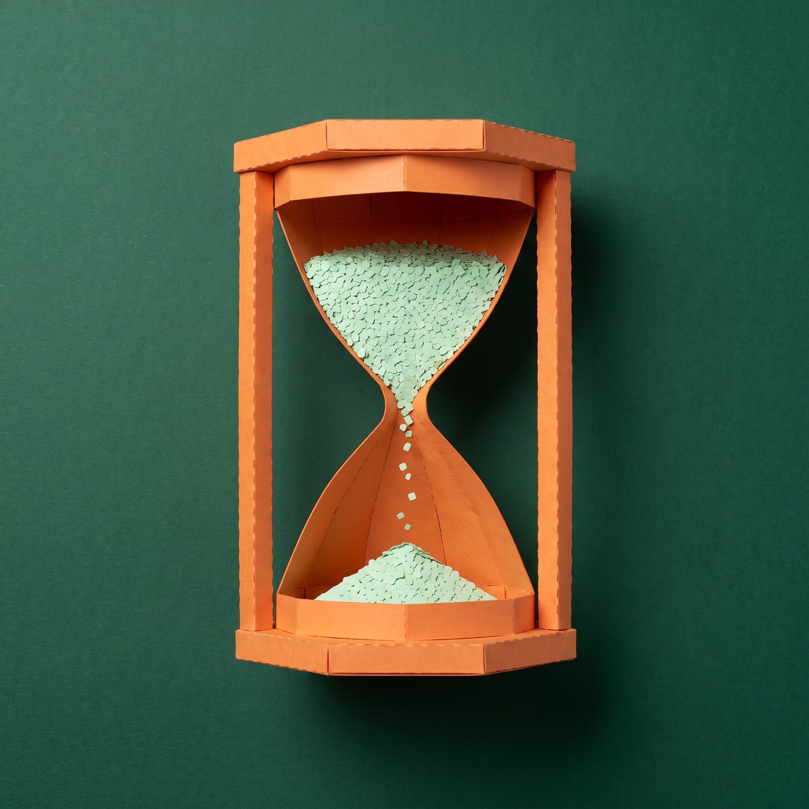 Paper sculpture of an hourglass with almost all its sand still in the top bulb, the first grains just starting to fall