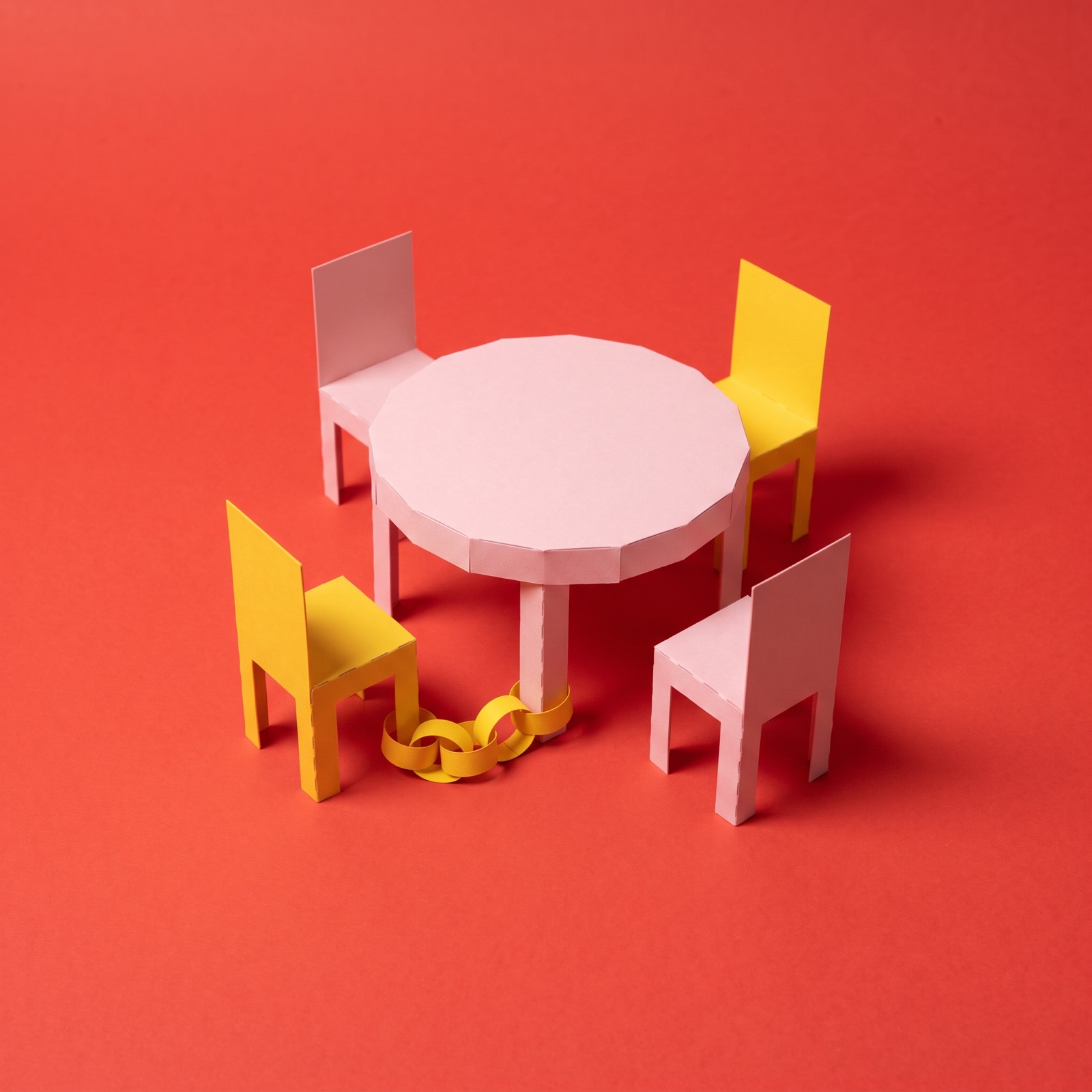 A round table with four chairs; one chair has a chain running from its leg to the table leg.